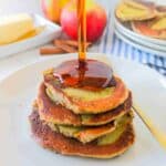 Syrup being poured onto protein pancakes on a white plate with a fork on it.