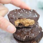 Fingers holding a chocolate almond butter protein cup on top of another.