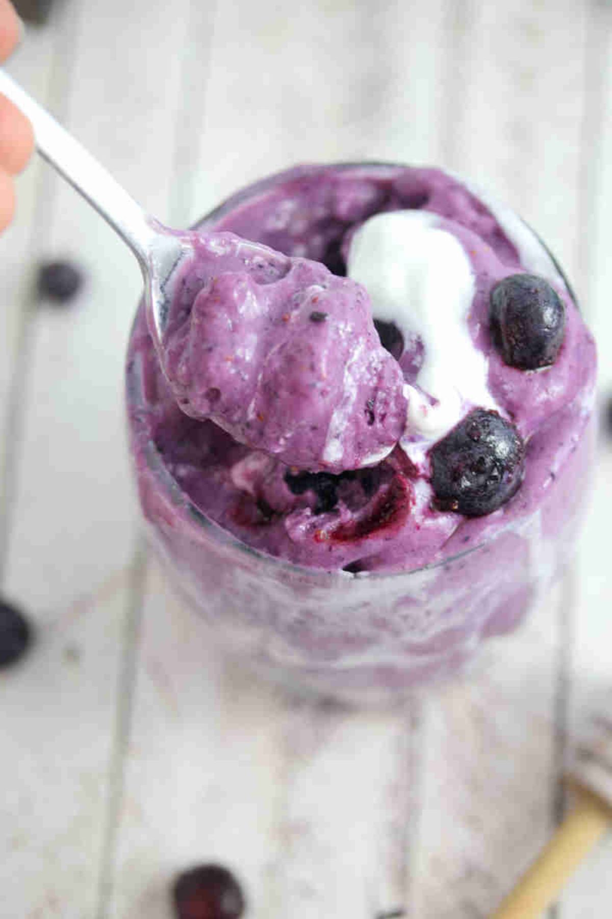 Blueberry protein fluff in a glass topped with coconut milk and a spoon in the glass.