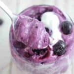 Blueberry protein fluff in a glass topped with coconut milk and a spoon in the glass.
