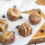 Chocolate protein balls drizzled with almond butter on parchment paper on a wooden cutting board with chocolate chips.