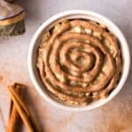 Creamy egg white oatmeal with cinnamon sugar drizzle in a white ramekin with cinnamon sticks behind it.