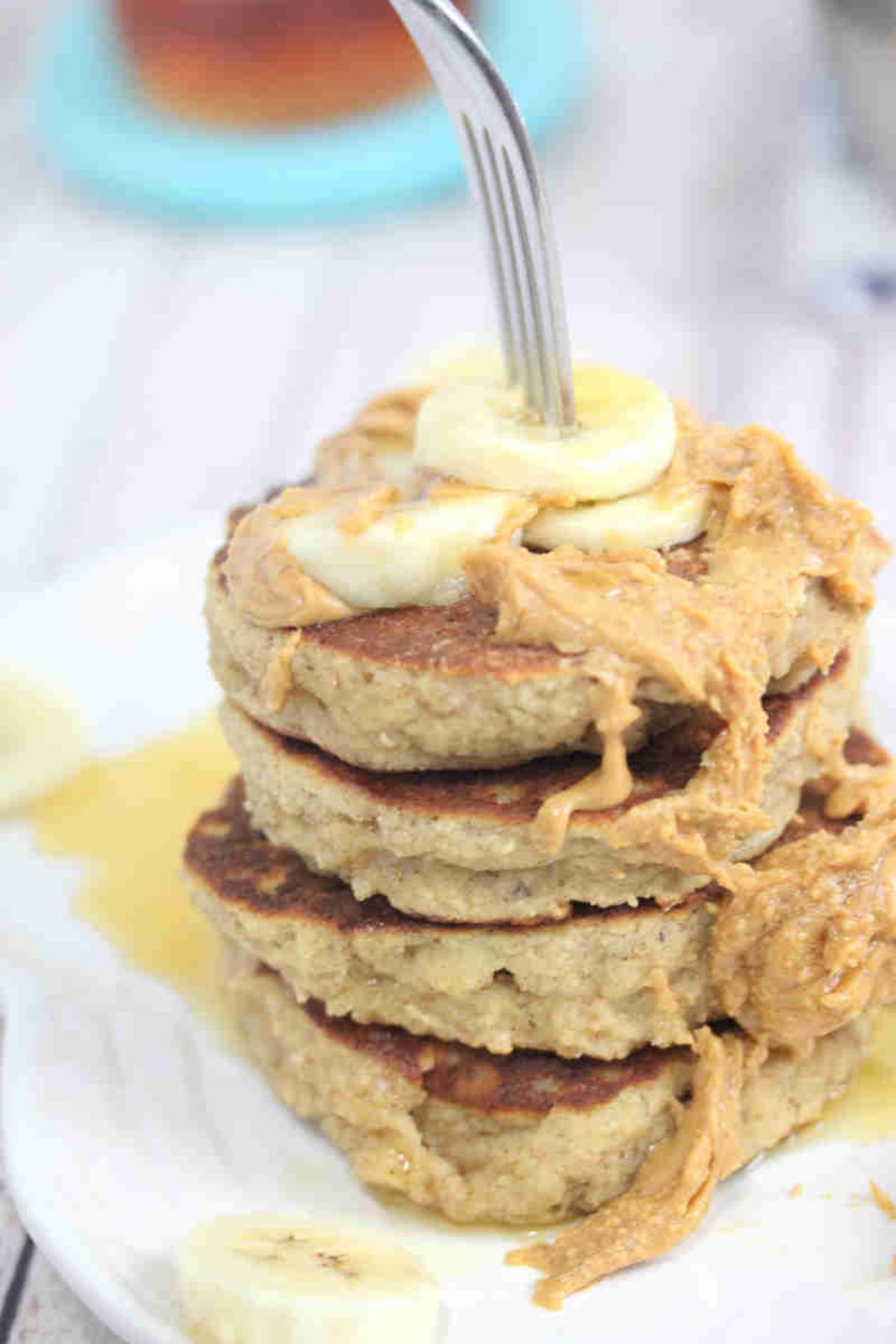 Stacked, gluten-free peanut butter pancakes topped with bananas and peanut butter on a white plate with a fork in it.