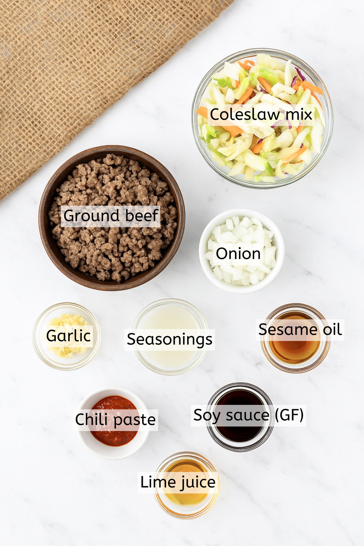 Ingredients like ground beef, seasonings, sesame oil, and coleslaw in bowls with text labels over top.
