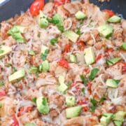 Cooked chicken skillet, with cheese, pepper, avocado and cilantro on it.