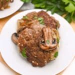 White plate with salisbury steak on it and a mushroom on top of them.