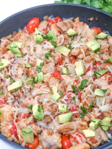 Cooked chicken skillet, with cheese, pepper, avocado and cilantro on it.
