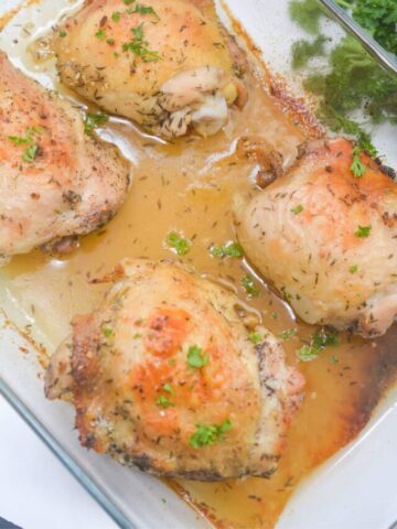 Cooked baked chicken thighs with parsley on top in a baking tray.