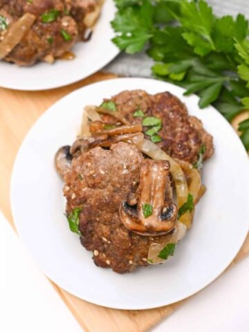 White plate with salisbury steak on it and a mushroom on top of them.