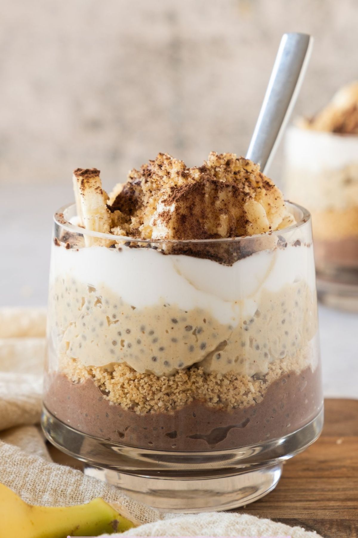 Chia pudding parfait in a glass layered with cookies, whipped cream, and bananas.