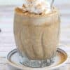 Blended overnight oats in a glass with whipped cream on top and a spoon in it and dusted with cinnamon.