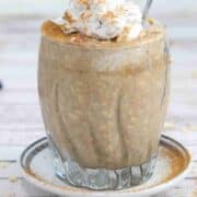 Blended overnight oats in a glass with whipped cream on top and a spoon in it and dusted with cinnamon.