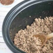 Cooked taco beef in a slow cooker with a wooden spoon in it.