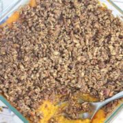 Sweet potato casserole with pecan topping in a glass baking dish with a spoon in the dish.