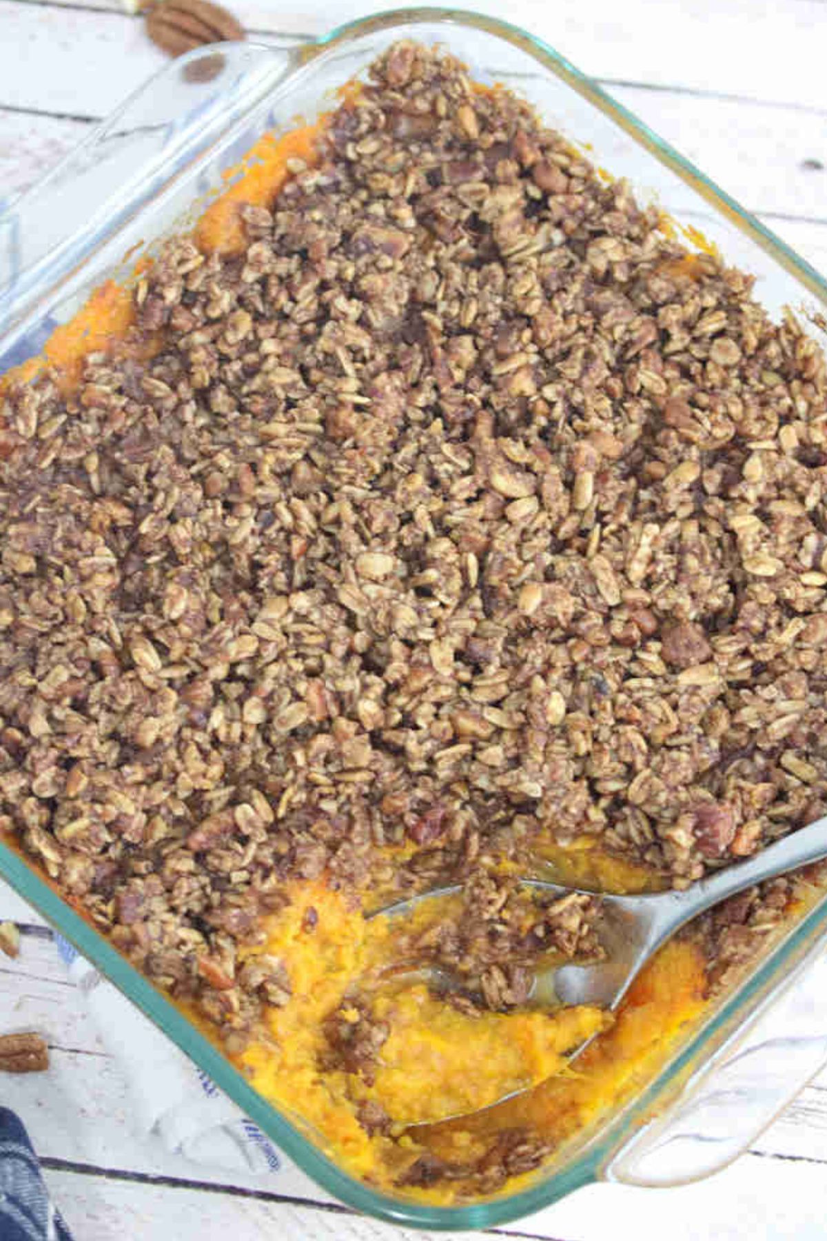 Sweet potato casserole with pecan topping in a glass baking dish with a spoon in the dish.