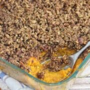 Sweet potato casserole with pecan topping in a glass baking dish with a spoon in the dish.