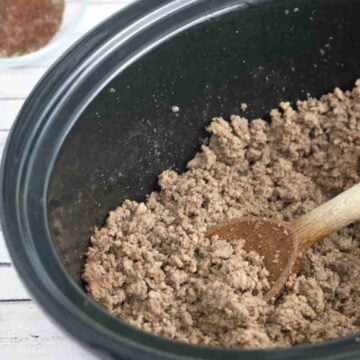 Cooked taco beef in a slow cooker with a wooden spoon in it.