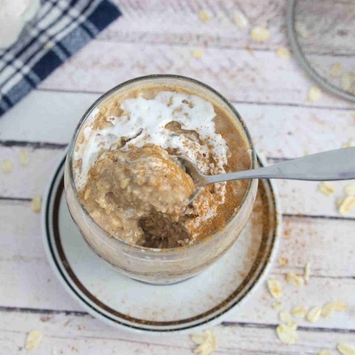 Blended overnight oats in a glass with whipped cream on top and a spoon in it and dusted with cinnamon.