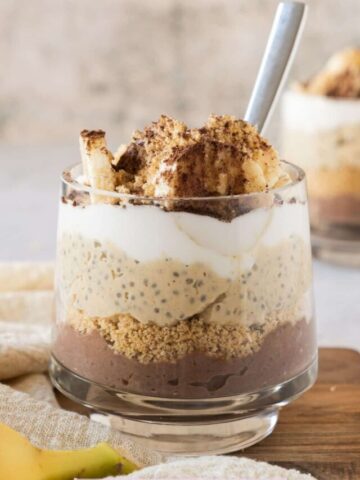 Chia pudding parfait in a glass layered with cookies, whipped cream, and bananas.