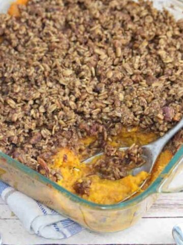 Sweet potato casserole with pecan topping in a glass baking dish with a spoon in the dish.