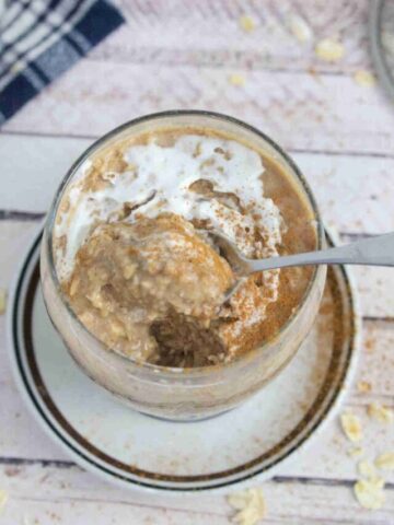 Blended overnight oats in a glass with whipped cream on top and a spoon in it and dusted with cinnamon.