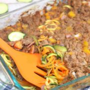 Beef and zucchini casserole topped with zucchinis in a baking dish with an orange spatula in the dish.