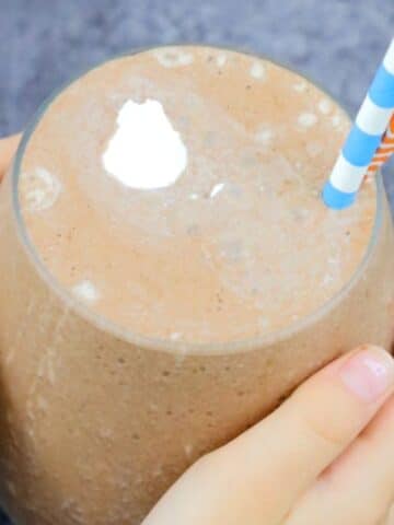Gut-healing chocolate smoothie in a glass with toddler hands holding it.