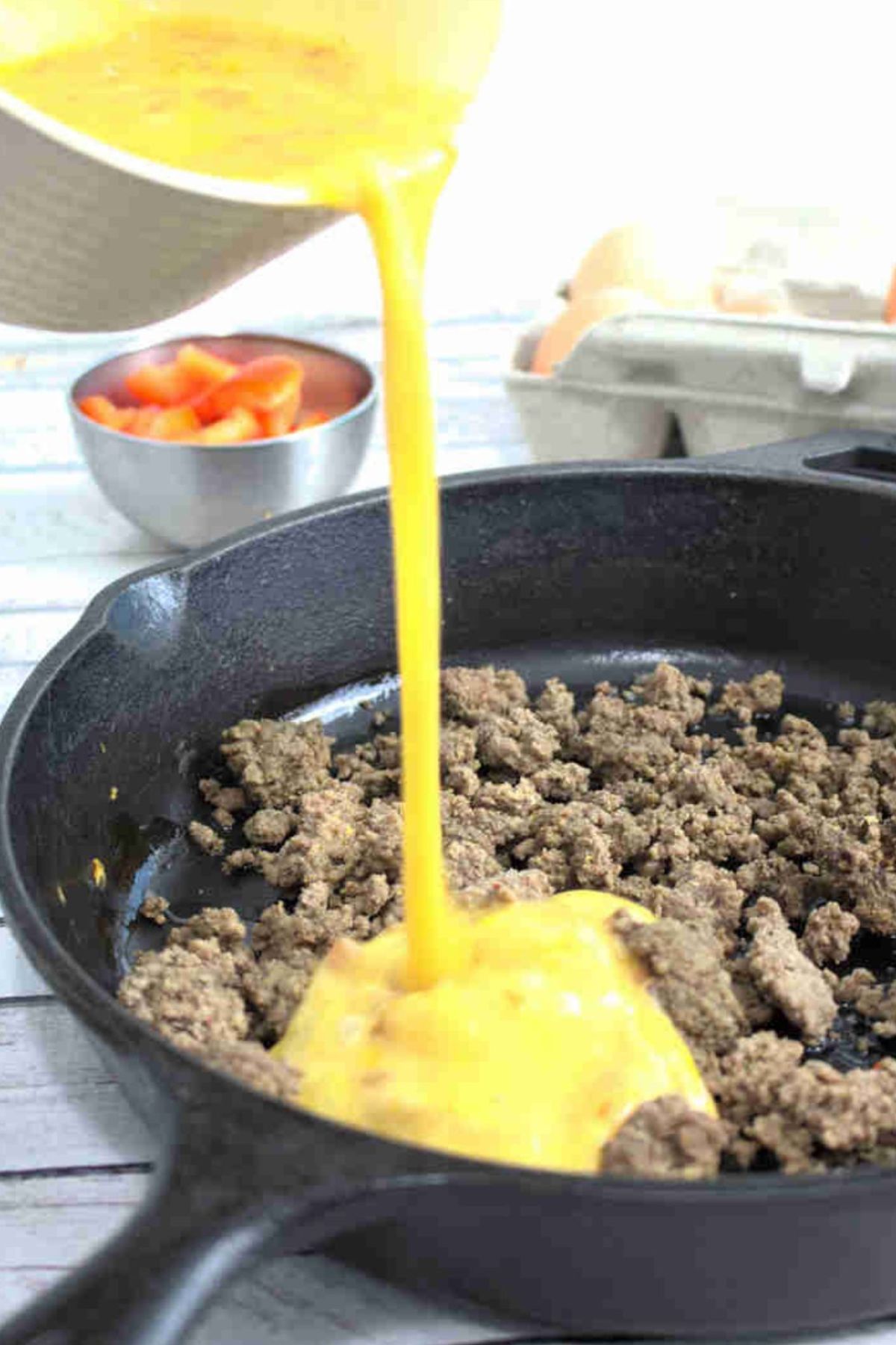 Scrambled eggs being poured into cooked ground beef in a cast iron pan.