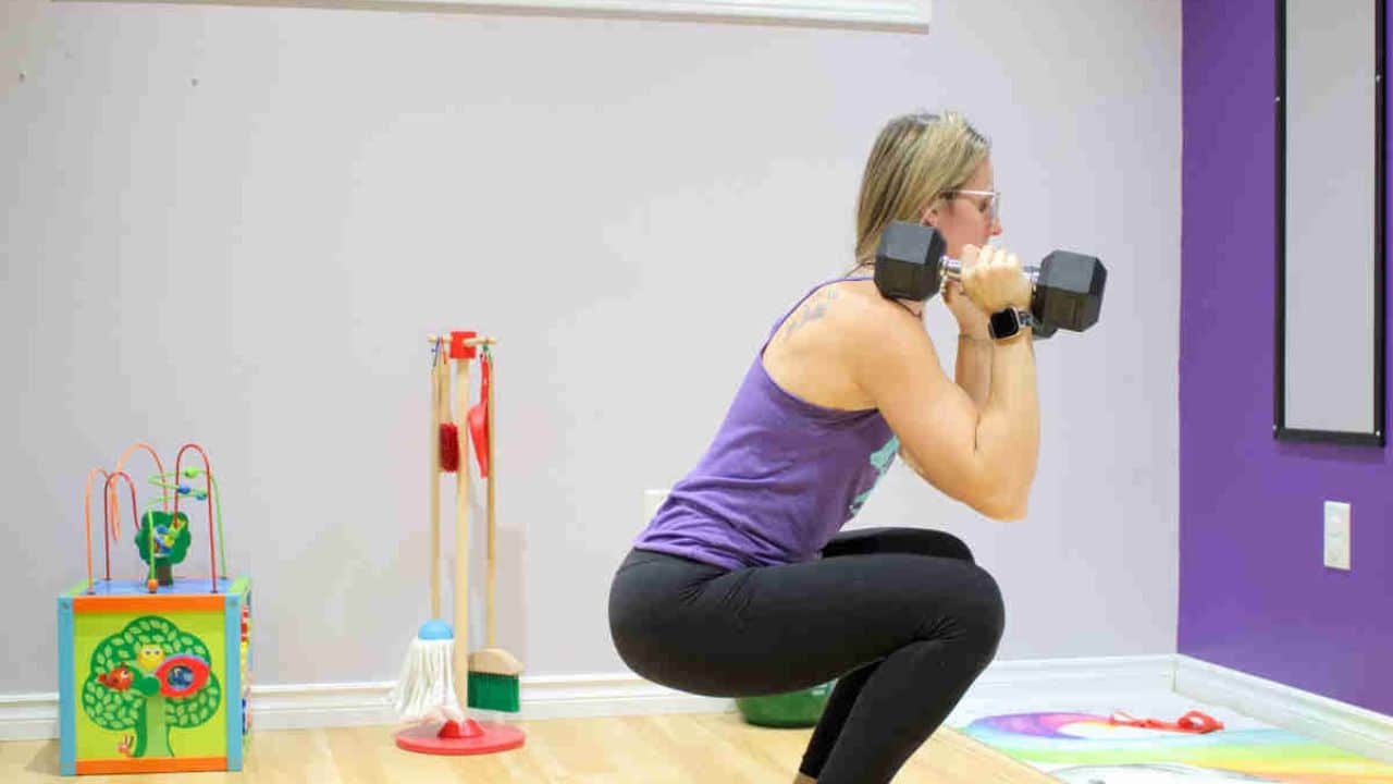 Woman in purple shirt with black pants performing a dumbbell squat.