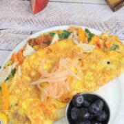 Chicken, pepper, and spinach omelet on a white plate with a side of blueberries and topped with kimchi.