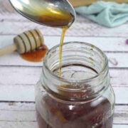 A spoon of homemade cough syrup being poured into a mason jar.