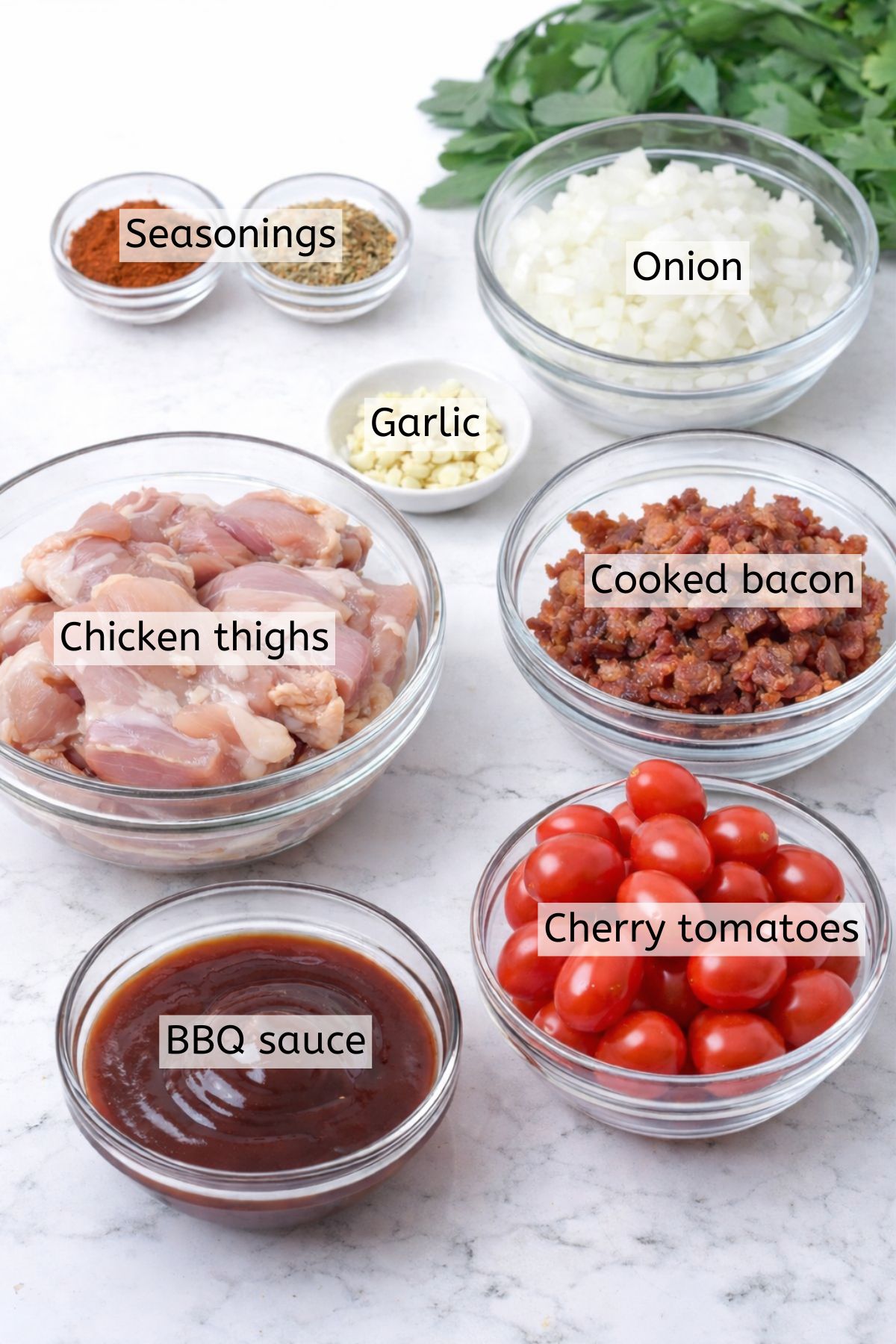 Multiple ingredients like bacon, chicken, sauce, and seasonings in glass bowls with text labels over top.