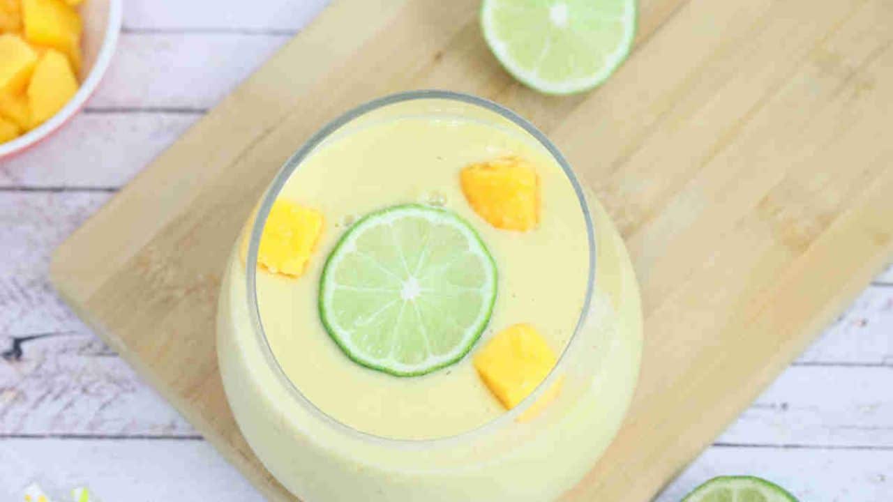 Mango smoothie in a glass with lime and mango on a cutting board.