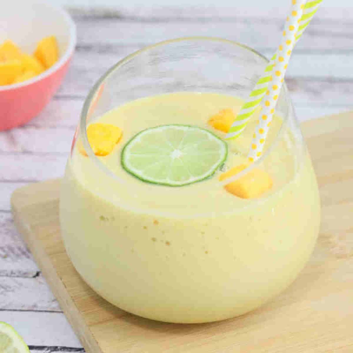Mango protein smoothie in a glass on a cutting board topped with lime and mango.