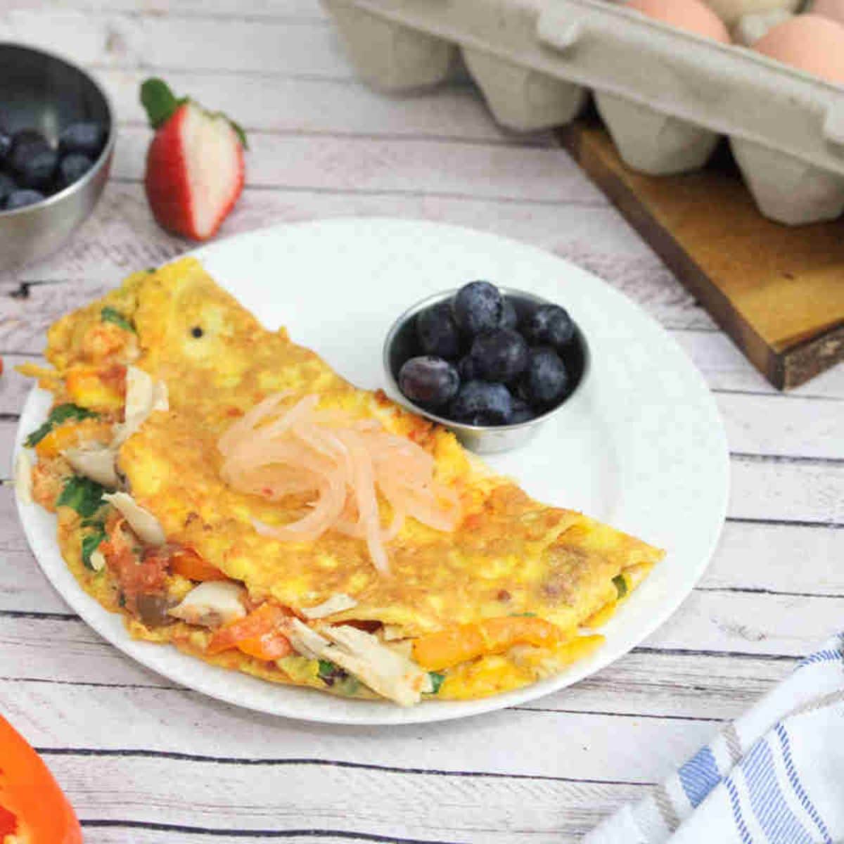 Chicken, pepper, and spinach omelet on a white plate with a side of blueberries and topped with kimchi.