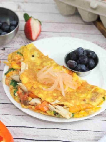 Chicken, pepper, and spinach omelet on a white plate with a side of blueberries and topped with kimchi.