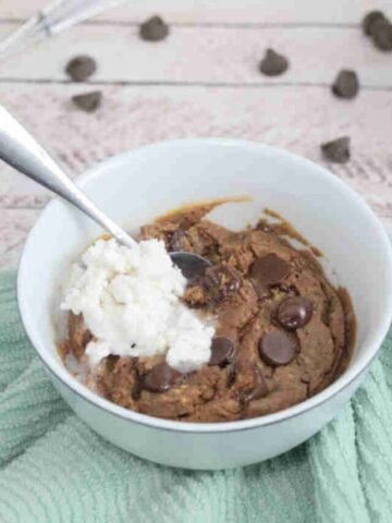 Chocolate brownie with chocolate chips in a white ramekin with coconut whip cream on top and a spoon in it.