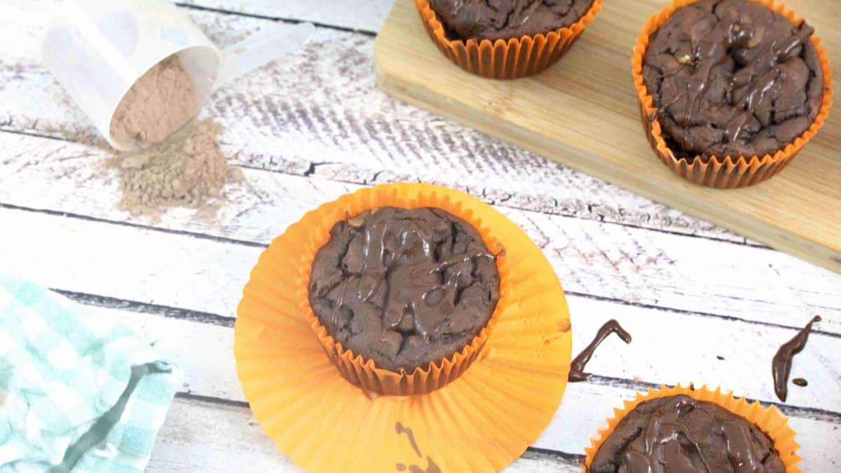 Chocolate protein muffins in orange muffin cups with protein powder around.