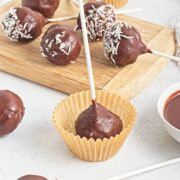 Chocolate dipped cake balls with sticks in them and topped with coconut.