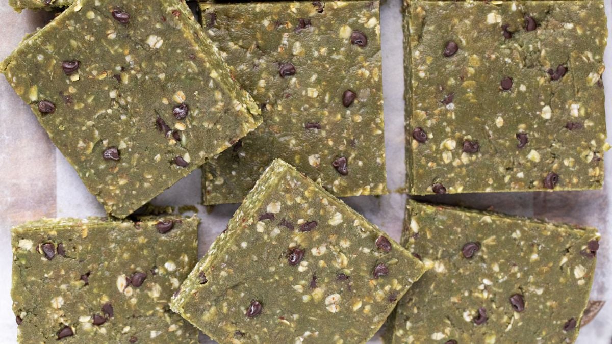 Three green vegan protein bars with matchinga in a bowl on an orange napkin behind it.