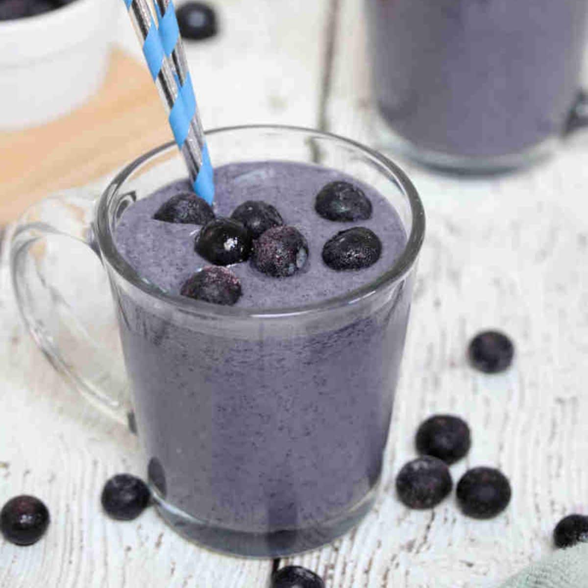 Blueberry protein shake in a glass with blueberries on top and straws in the glass.
