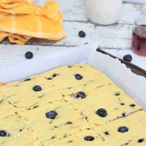 Sheet pan blueberry pancakes on parchment paper sliced, with a linen and milk behind it.