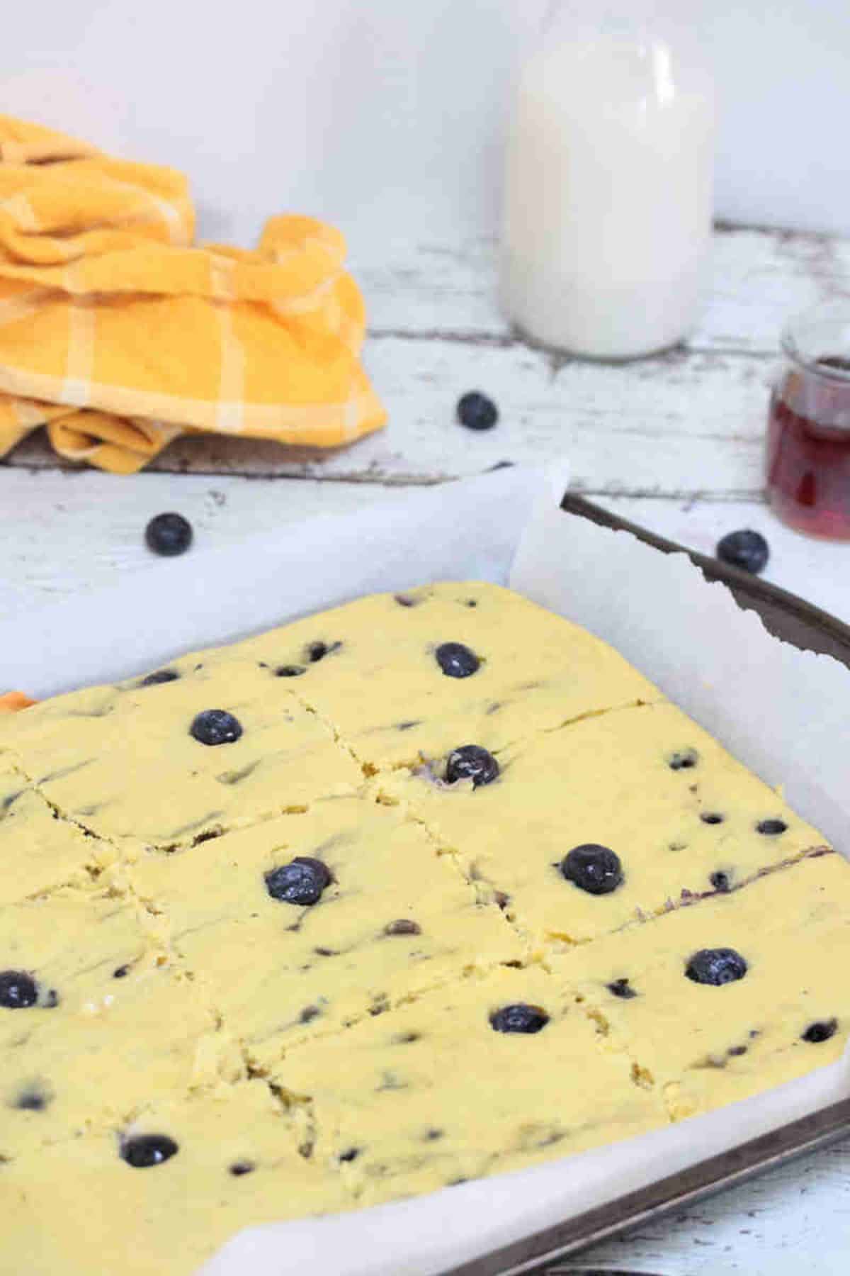 Sheet pan blueberry pancakes on parchment paper sliced, with a linen and milk behind it.