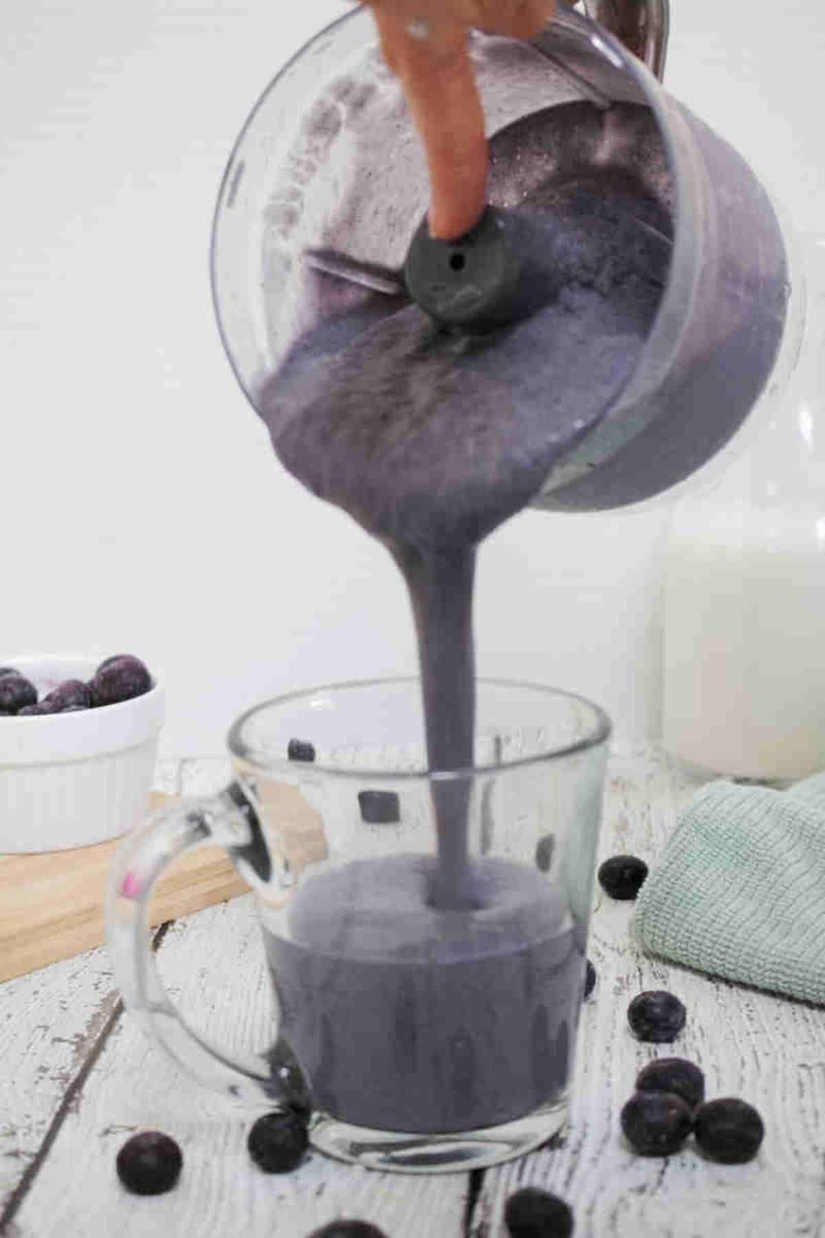 Blueberry protein shake being poured into a glass.
