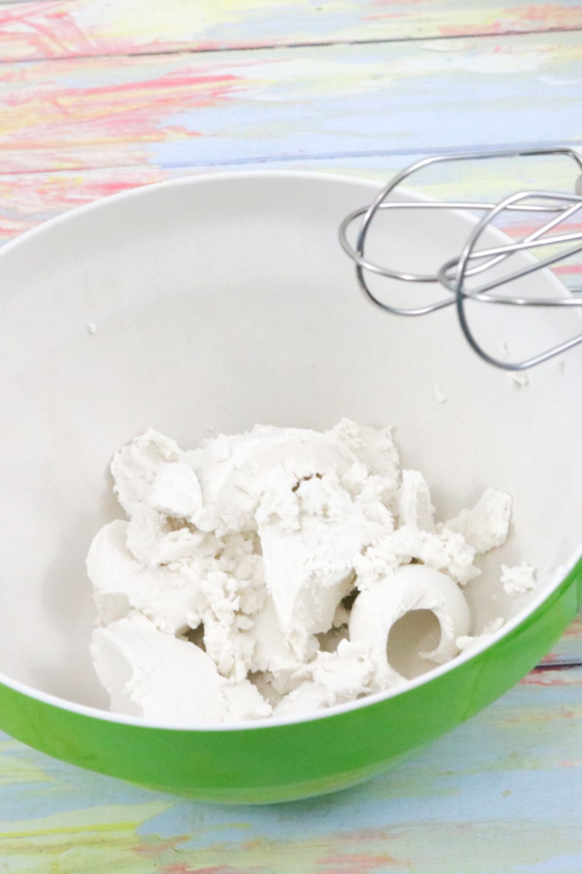 Coconut cream in a green bowl with a handheld mixer over the top.