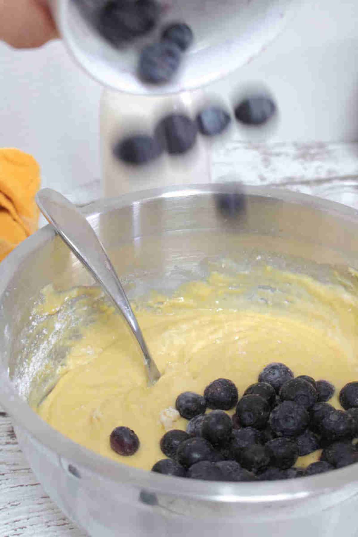 Steel bowl with raw pancake batter, blueberries and a fork.