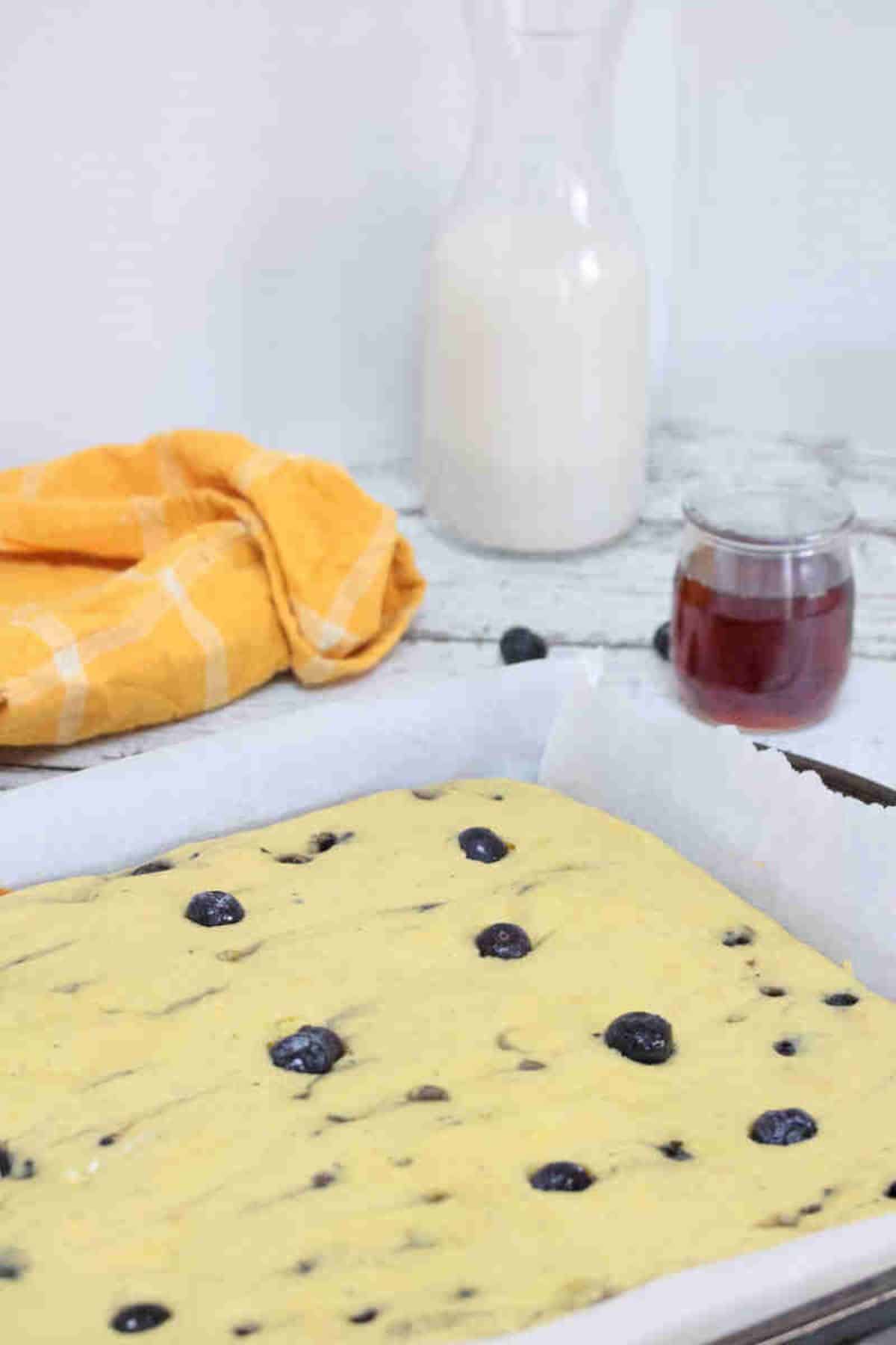 Blueberry protein pancakes on a parchment paper lined baking sheet with milk and maple syrup behind it.
