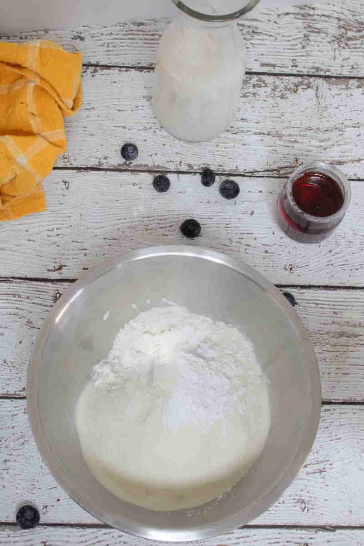 Flour in a steel bowl with maple syrup and milk behind it.