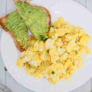 Dairy-free scrambled eggs on a white plate with avocado toast beside them.