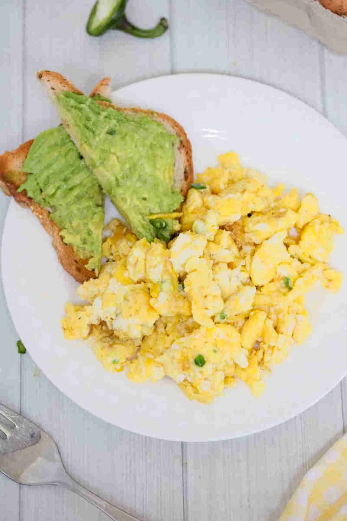 Dairy-free scrambled eggs on a white plate with avocado toast beside them.